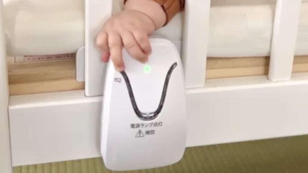 柵のすき間から手をのばしてベビーセンスホームの本体をさわる赤ちゃん